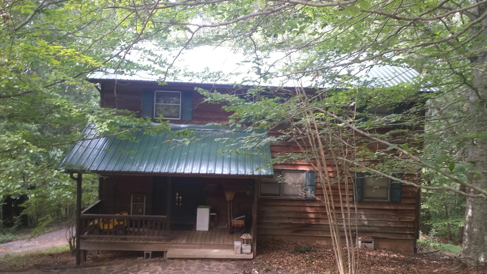 Green metal roof and covered porch on a log cabin in Milford