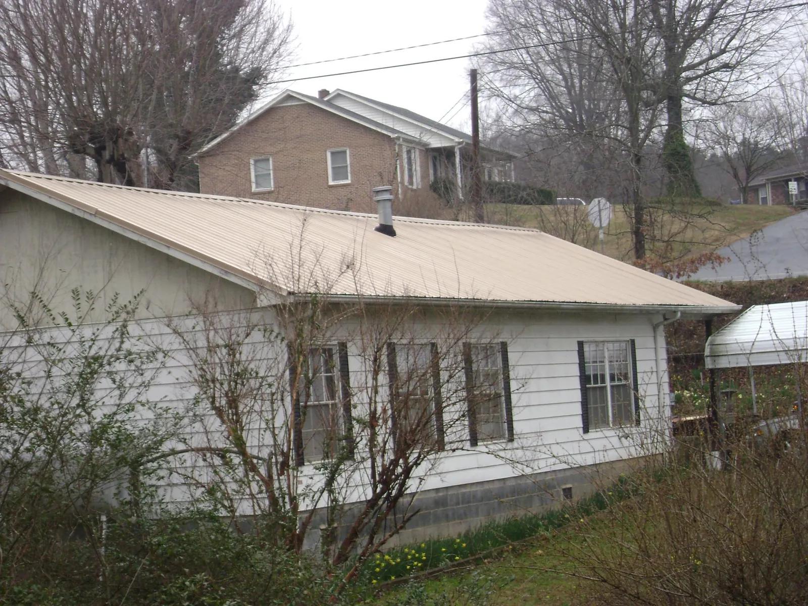 Tan metal roof on a white sided house set into a hillside — Commercial Roofing by Roofing Brothers in Milford